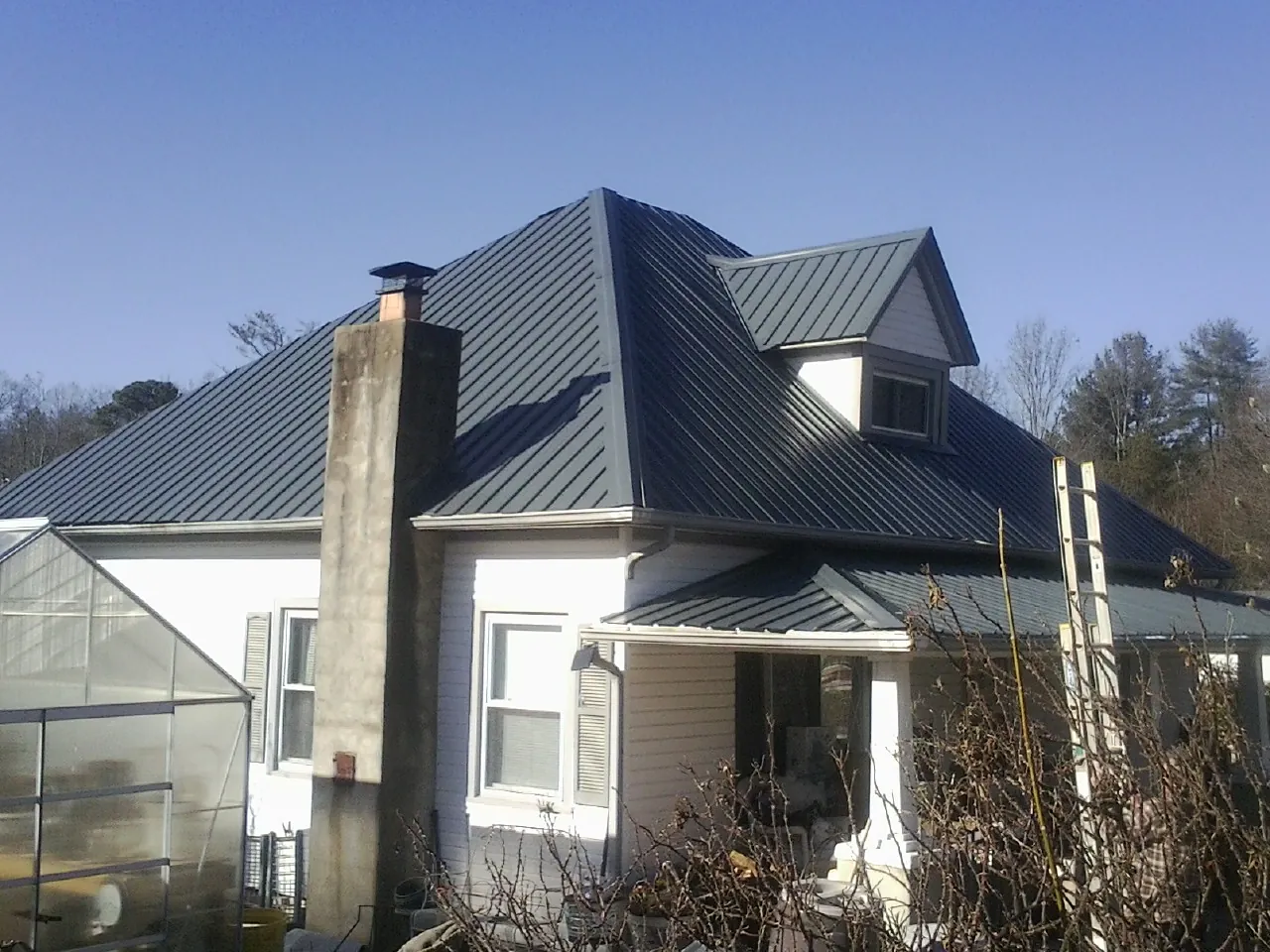 Dark blue standing seam metal roof on a white farmhouse with dormer — Slate & Tile Roof Repair by Roofing Brothers in Monona