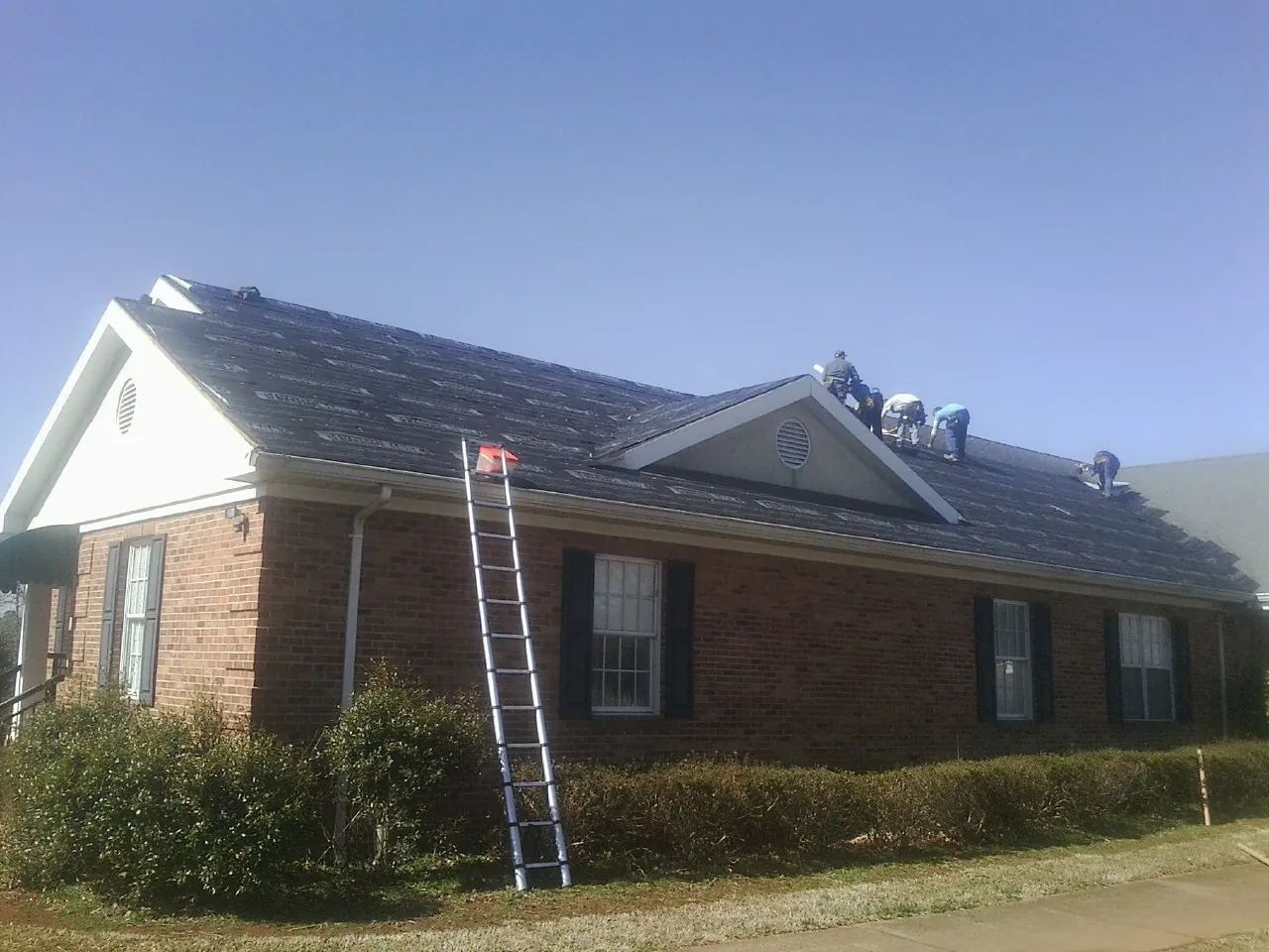 Crew tearing shingles off a brick ranch roof with a ladder set — Emergency Roof Repair work by our crew in Monona