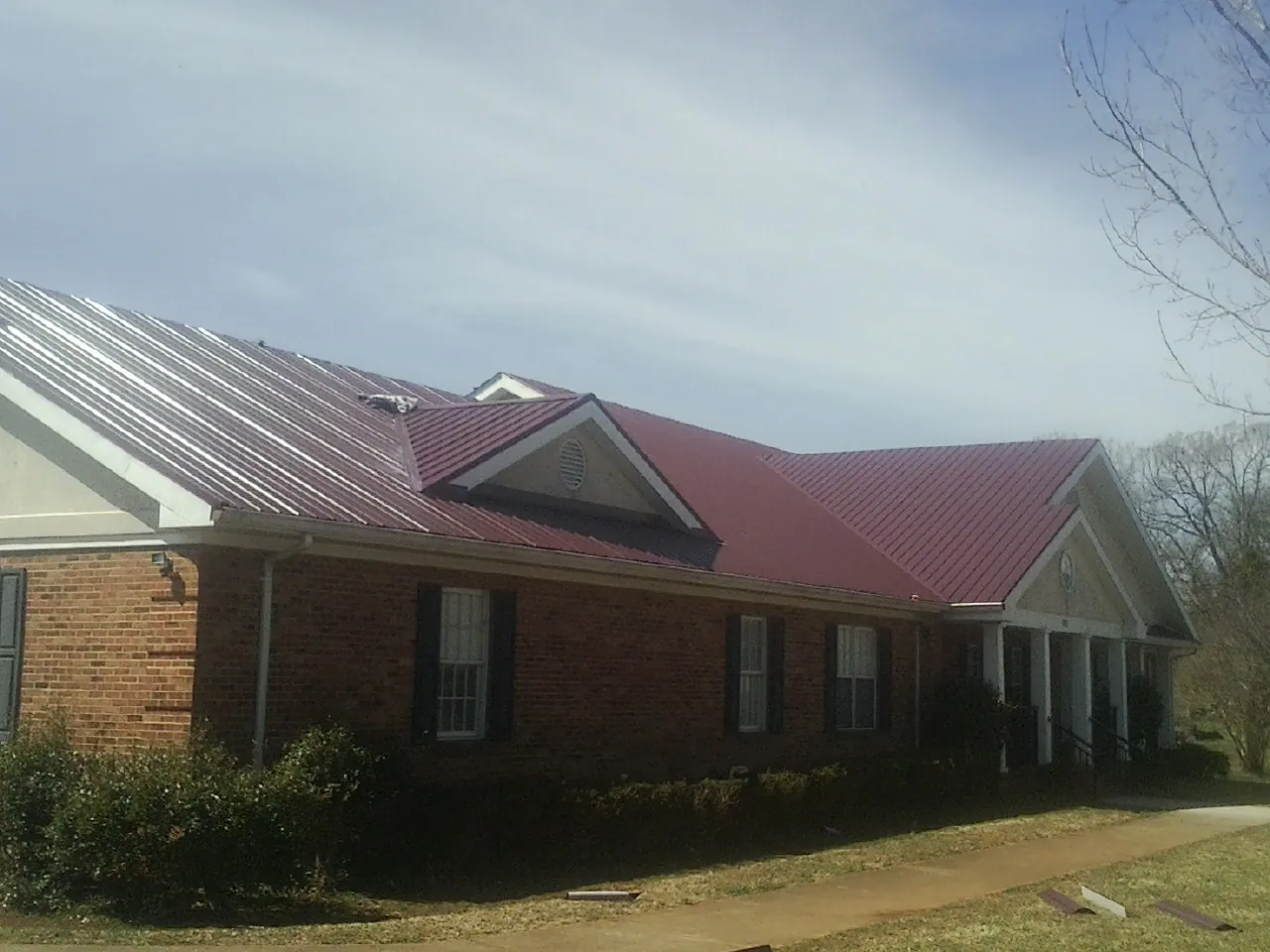 Red metal roof with gabled entries on a long brick building, from a Hail Damage Roof Repair job in Monona