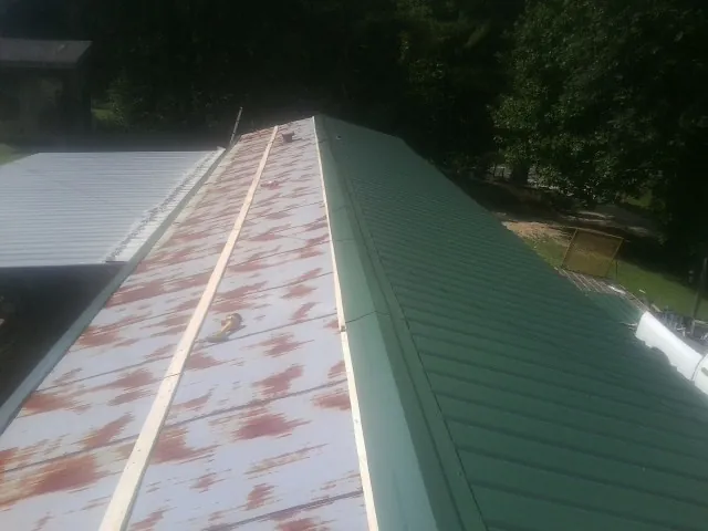 Old rusted panels beside newly installed green metal roofing — Wind Damage Roof Repair by Roofing Brothers in Monona