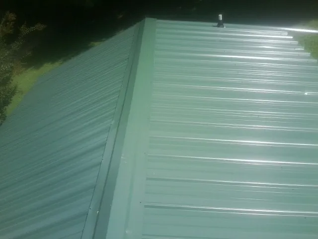 New green metal panels meeting at the ridge of a roof — Flat Roof Repair work by our crew in Monona