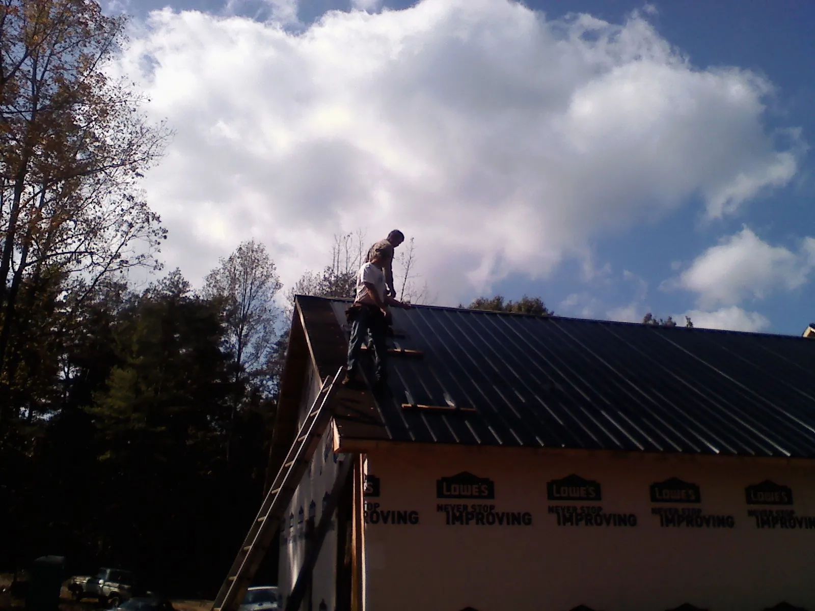 Roofer fastening dark metal panels high against a cloudy sky, from a Roof Inspection job in Monona