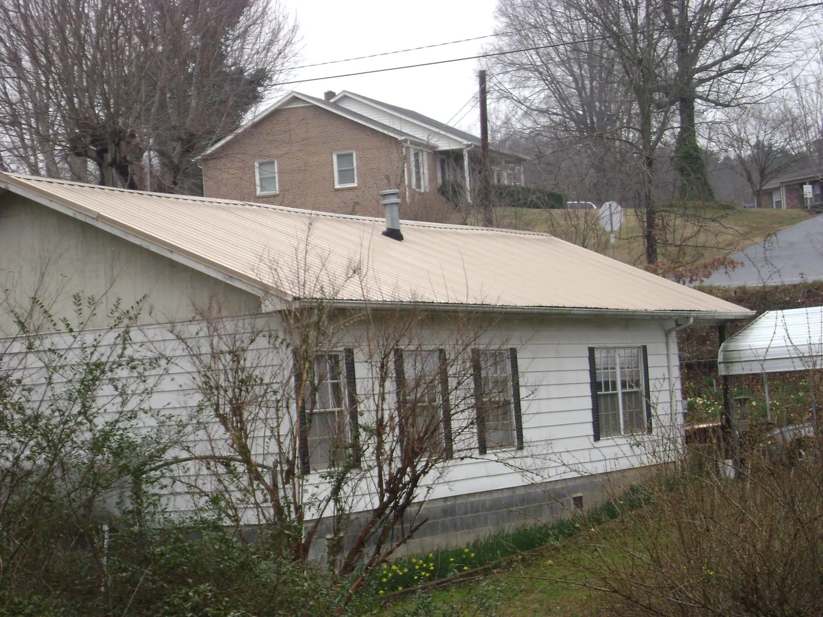 Tan metal roof on a white sided house set into a hillside — Commercial Roofing by Roofing Brothers in Monona