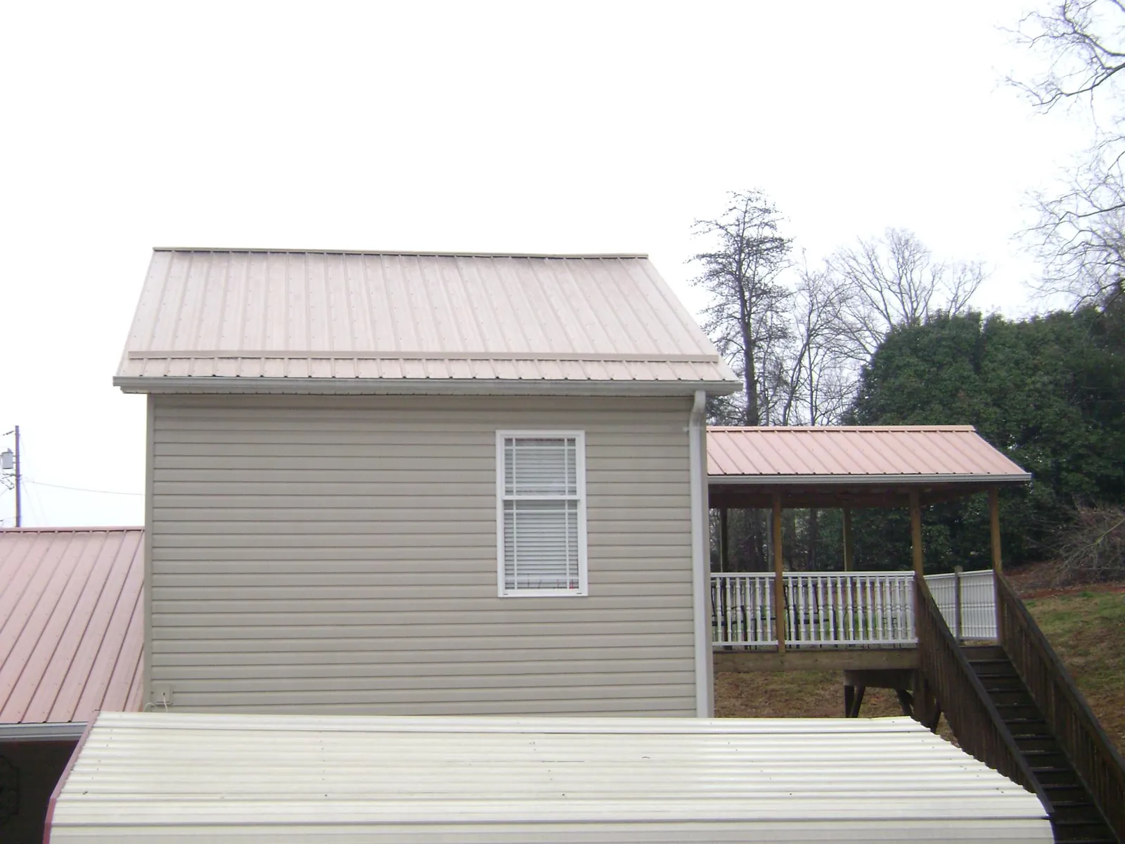 Tan metal roofs on a two story addition and attached porch, from a Roof Replacement job in Monona